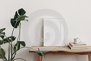 White portrait frame mockups on vintage bench, table. Cup of coffee on pile of books and monstera potted plant. White