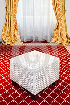 White pouf in the room with vintage red carpet and yellow drapes