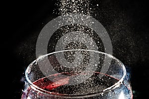 White powder falling into a transparent glass cup filled with wine. Isolated on dark background