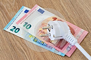 White power plug over euro banknotes on a brown wooden surface. Expensive energy and cost of electricity concepts