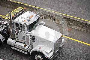 White powerful big rig semi truck with oversize load sign on the roof running on the highway road to point of loading oversized