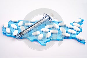 White pharmaceutical pills and syringe over map of America background