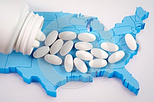 White prescription pills spilling from medicine bottle over map of America