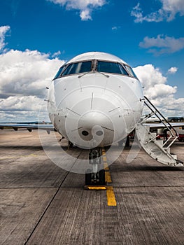 White private airplane closeup with folding ladder standing on the aerodrome field on a background of blue sky