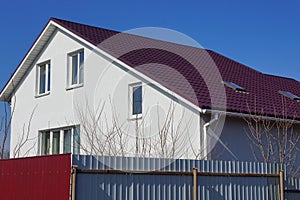 White private house with windows under a red tiled roof behind a gray metal fence