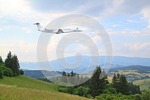 White private jet business jet flies against backdrop of  summer forrest, meadows and fields countryside landscape in Slovakia