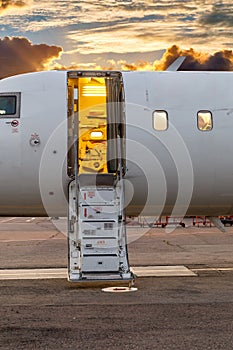 White private jet and open ladder at the airport against the background of dramatic sky and sunset