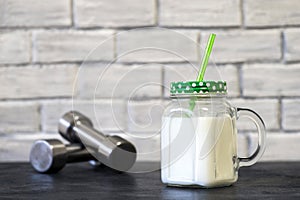 White protein cocktail in a mug on the background of dumbbells and a white wall decorated with bricks. Background