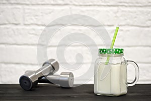 White protein cocktail in a mug on the background of dumbbells and a white wall decorated with bricks. Background