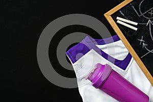 White and Purple Sports Uniform and Water Bottle Next to a Chalkboard on Black Background