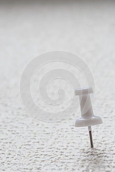 A white push pin is pinned on a white surface.