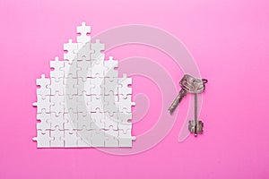 White puzzle. House shape puzzle and keys. The concept of rent, mortgage. Pink background. Top view