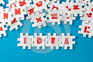 White puzzle jigsaws with alphabets building word IDEA at the center of other alphabets on blue background, business idea,