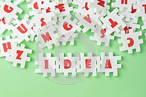 White puzzle jigsaws with alphabets building word IDEA at the center of other alphabets on green background, business idea,