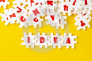 White puzzle jigsaws with alphabets building word IDEA at the center of other alphabets on yellow background, business idea,