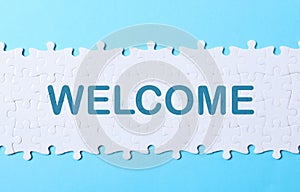 White puzzle pieces and word WELCOME on light blue background, top view