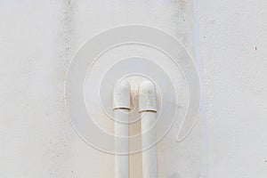 White PVC pipes emerge from a gray concrete wall.