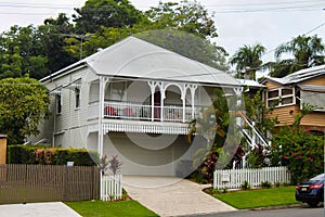 White queenslander home with tropical greenery and tall trees on overcast day in Australia