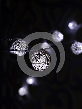 White rattan balls light garland. New Year`s garland. Christmas led lights on dark background. Blurred glowing light bulb garland