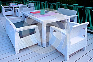 white rattan wicker armchairs and tables on summer terrace in twilight