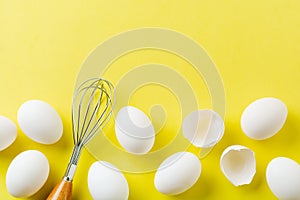 White raw chicken eggs lying in horizontal row with broken egg on yellow background.