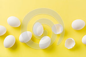 White raw chicken eggs lying in horizontal row with broken egg on yellow background