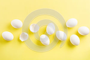 White raw chicken eggs lying in horizontal row with broken egg on yellow background.