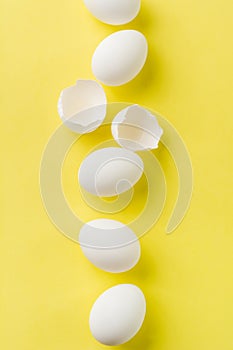 White raw chicken eggs lying in vertical row with broken egg on yellow background.