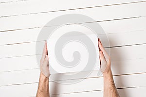 White rectangular box in male hands. Top view. White table on the background