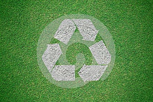 White recycle logo painted on green grass field from top view. R