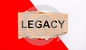 On a white and red background, brown torn cardboard with the text LEGACY