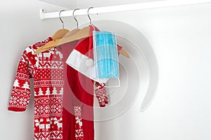 White and red christmas pajamas, hat, tights and face mask hanging on wooden hangers inside a white closet. Holidays during