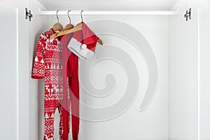 White and red christmas pajamas, hat and tights hanging on a wooden hangers on the left of a white closet