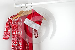 White and red christmas pajamas, hat and tights hanging on a wooden hangers on the left of a white closet