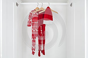 White and red christmas pajamas, hat and tights hanging on a wooden hangers in the middle of a white closet