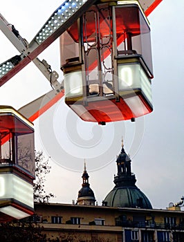 White and red clear glass gondola and detail of giant Ferris wheel in Budapest with church tower in the background