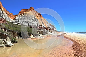 White and red cliffs near the sea at Morro Branco, Ceara, Brasil. At the base clear water stream and blue clear sky at the horizon
