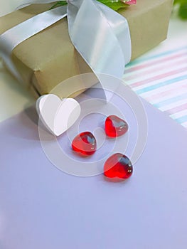 White and red hearts in front of gift box on lavender paper background.