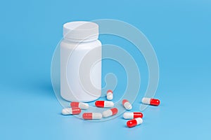 White and red pills, tablets and white bottle on blue background.