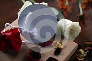 White and red roses, dried petals with blank tag label paper for your notes on a gift of a book on messy table.  Still life.