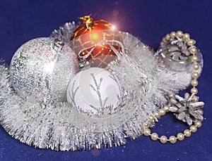 White, red and silver glass New Year`s balls, brilliant tinsel, cones and a pearl beads on a blue background - New Year`s composit