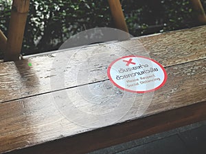 The white and red sticker labeled `Please respect social distancing` is placed on a long bench in the park.