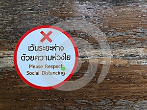 The white and red sticker labeled `Please respect social distancing` is placed on a long bench in the park.