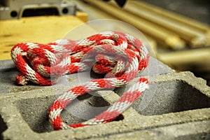 White and red thick heavyweight nylon rope sitting casually atop cement blocks in a workshop.