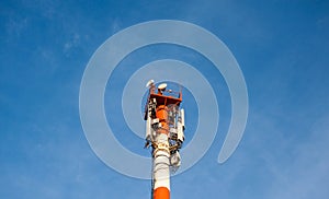 A white and red tower with cellular communication antennas on a sky