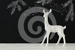 White reindeer on wooden table over chalkboard background whith hand drawn chalk illustrations.