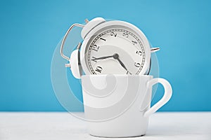 White retro alarm clock in cup on blue background. Morning time concept
