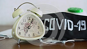 White retro alarm clock ringing on brown wooden desk near black protective face masks with word COVID-19 close up