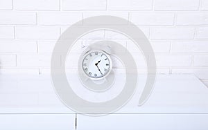 White retro alarm clock with twenty five minutes past one o`clock near brick wall on white workplace