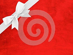 white ribbon bow wrapped around corner of bright red paper with abstract striped pattern